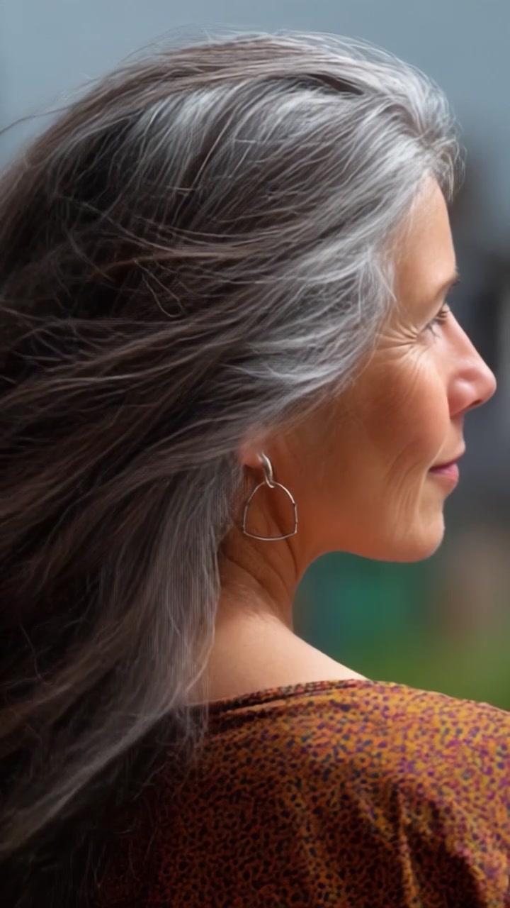 Retrato de una Mujer con Cabello Plateado Suelto y Pendientes en Forma de Corazón, Capturado en Dos Marcos, Mostrando su Elegante Perfil y Belleza Natural