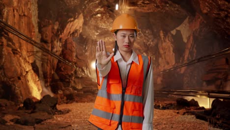 asian female engineer with safety helmet disapproving with no hand sign in underground mine tunnel