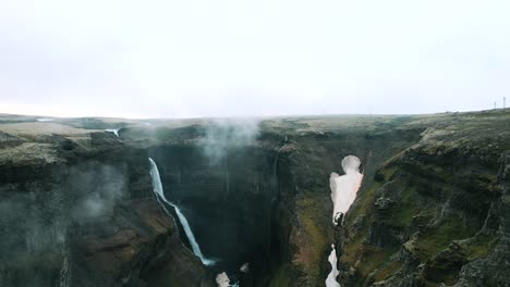 Drone shot revealing vast landscape of Haifoss waterfall surrounded by fog, Iceland
