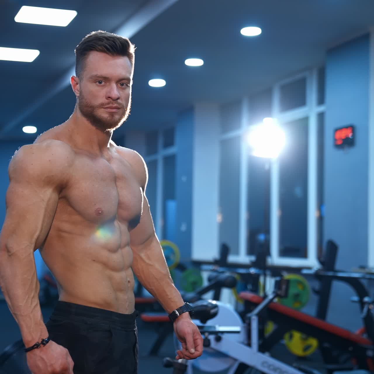 Hot handsome strong guy man without a shirt against gym background. Male beauty concept. Slow motion