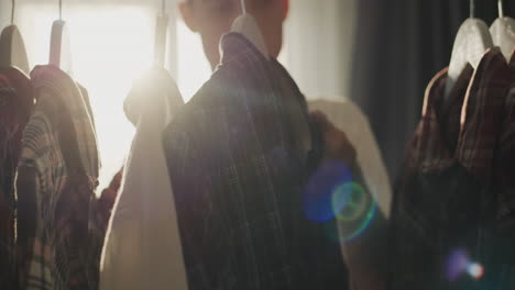 a man chooses his clothes near a rack with a coat hanger, from behind he is illuminated by the sun's rays from the window