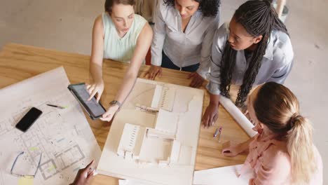 diverse female architects discussing architectural model and blueprints at work, in slow motion