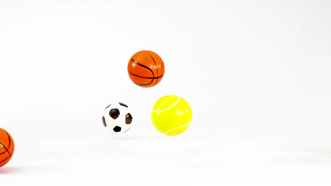 Small soccer balls, basketballs, and tennis balls fall and bounce against a plain white background