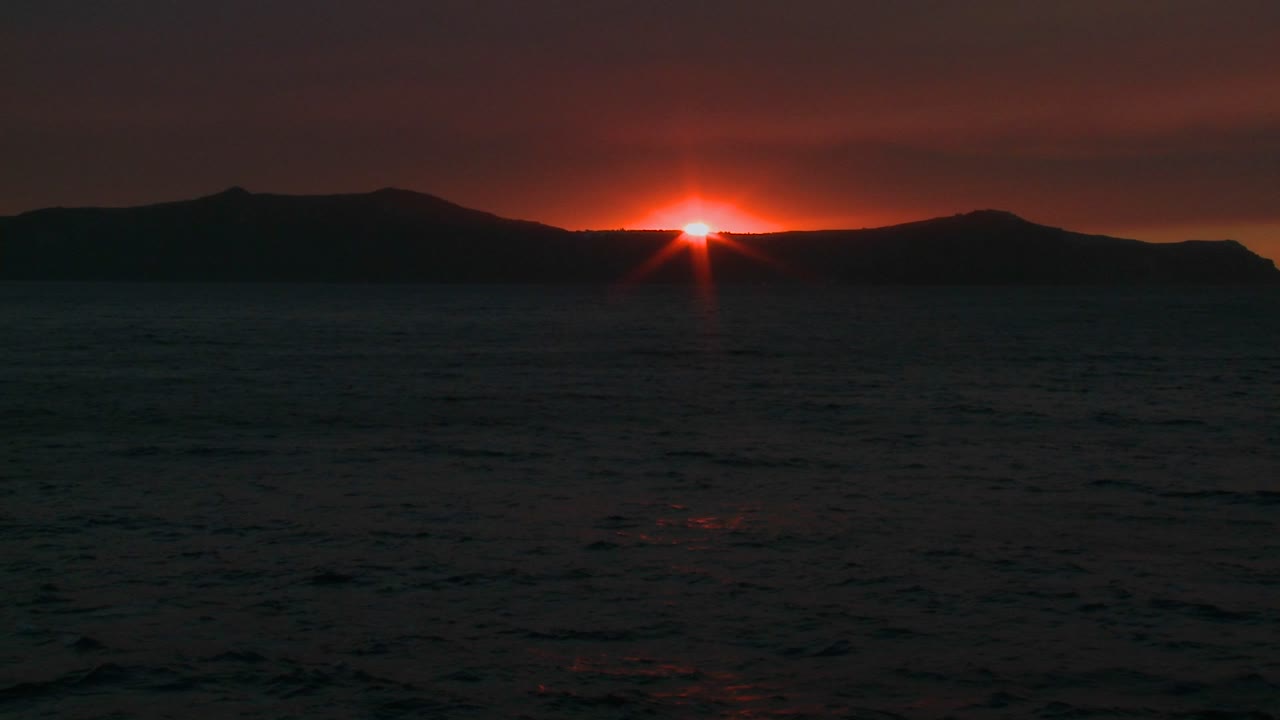 Die Sonne geht hinter einer Insel im Meer unter.
