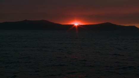 the sun sets behind an island in the ocean