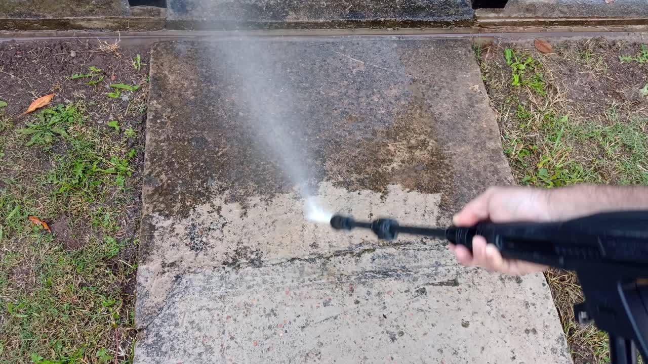 Pressure washer using water to clean dirty sidewalk of house, close up