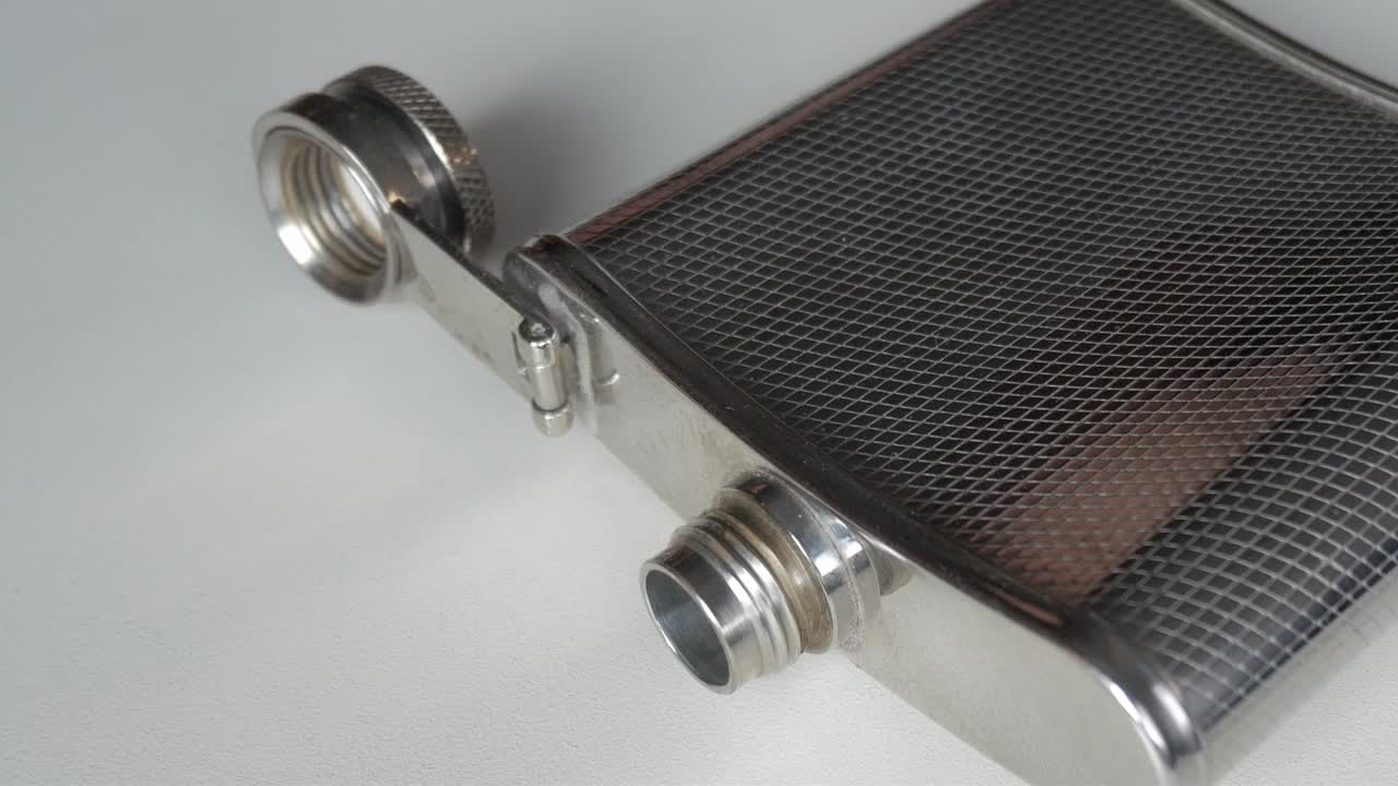 Close-up of metallic flask with textured design on white background, zoom out
