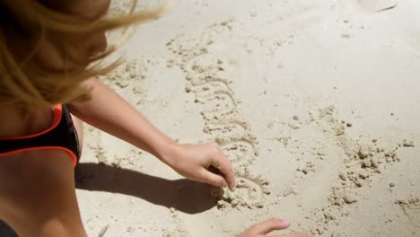 Niña-Escribiendo-Su-Nombre-En-La-Arena-De-La-Playa-4k