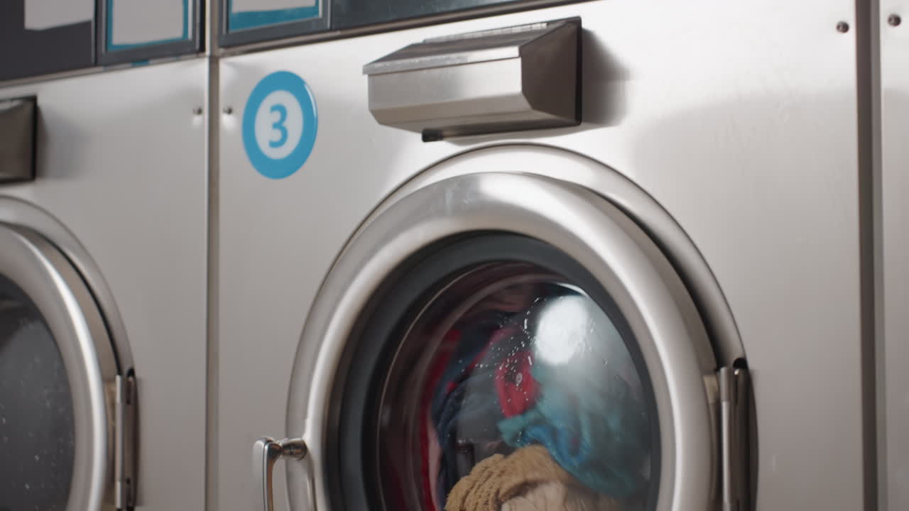 Industrial washing machines with upper and lower units running, clothes and shoes rotating behind round glass doors, stainless frames, smooth motion showing cleaning cycle with water and detergent