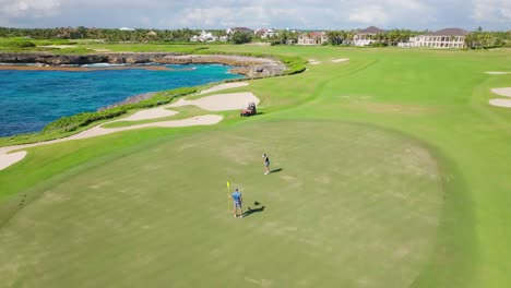 Aerial-orbiting-shot-of-couple-playing-golf-on-luxury-golf-course-with-Caribbean-Sea-in-background