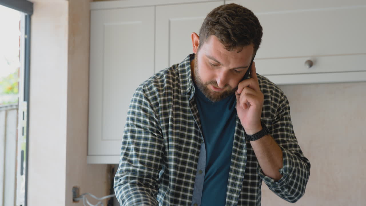 Hombre renovando la cocina en casa, mirando muestras de pintura y hablando por el teléfono móvil.