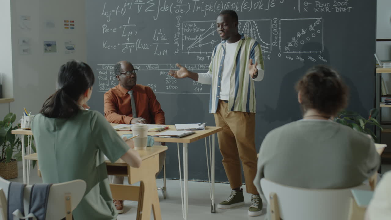 Students attending a lecture in a classroom with a professor presenting complex formulas on a blackboard