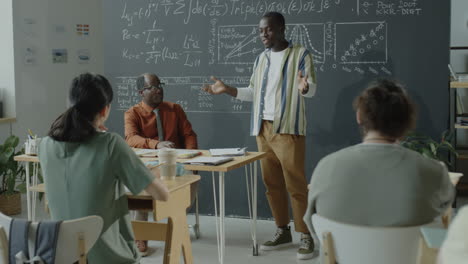 students attending a lecture in a classroom with a professor presenting complex formulas on a blackboard