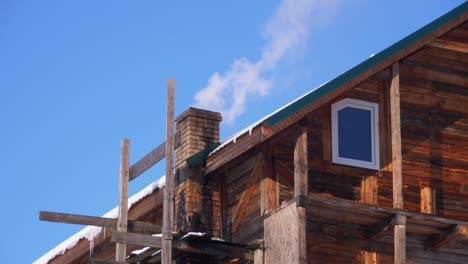 smoke from a brick chimney on a roof of wooden house in winter against a blue sky