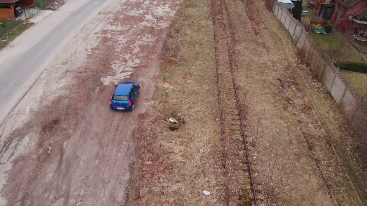 Un'auto blu percorre binari ferroviari abbandonati