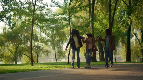 Parents-holding-kid-skateboarding-in-green-sunny-park.-Caring-people-together.