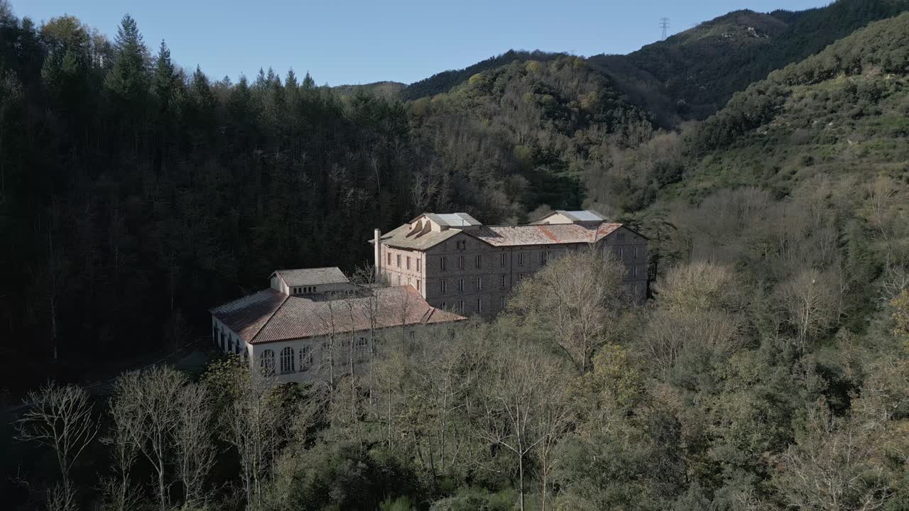 Font picant spa, an antique building in a wooded valley in sant hilari sacalm, girona, catalonia, shows signs of decay and neglect, surrounded by trees and hills under a clear blue sky