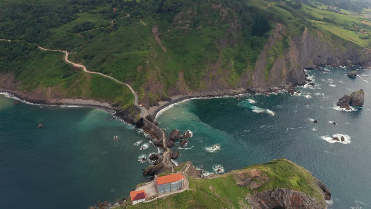 Oceano increspato vicino a una montagna verde con un sentiero sotto il cielo