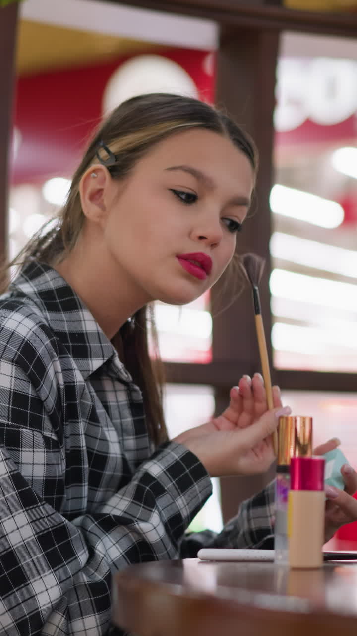 adolescente latina concentrada maquillándose en una mesa, perfil concentrado usando un pincel y un espejo compacto con un frasco de base y plantas al fondo, iluminación interior cálida y brillo natural sutil