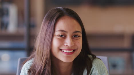 Millennial-Asian-female-creative-sitting-in-an-office-smiling-to-camera,-close-up