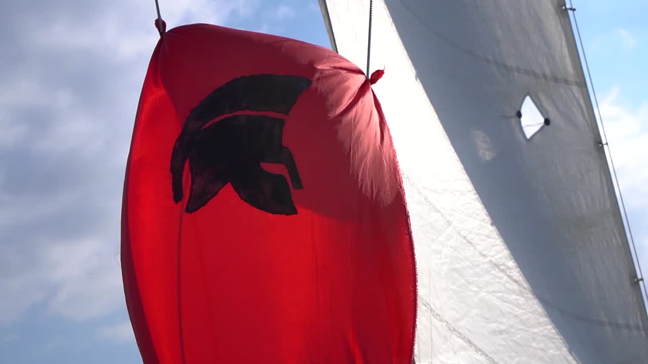 Bandeira espartana vermelha tremulando ao vento em um veleiro durante um dia ensolarado.