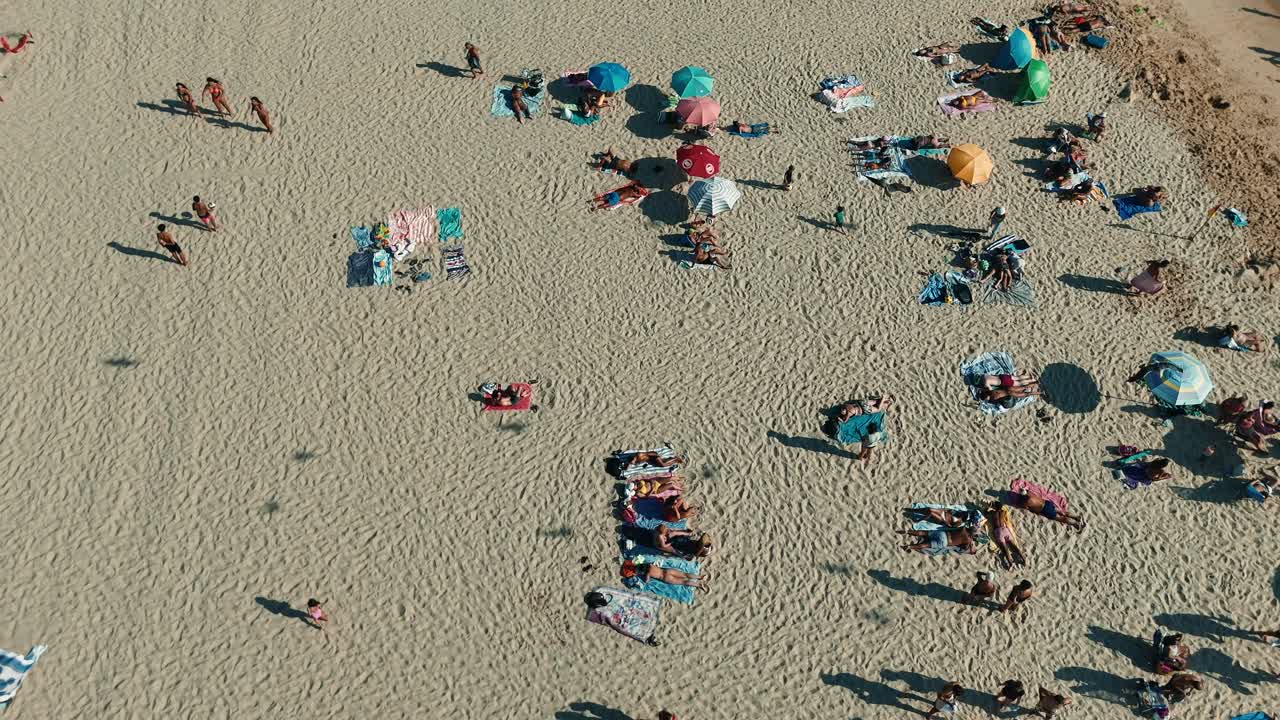 Aerial view of a sandy beach with people relaxing under umbrellas
