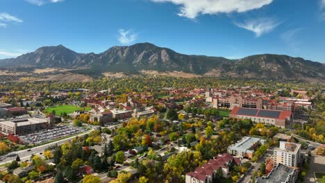 aerial drone moving towards the university of colorado boulder on a sunny fall day with bright leaves and flatiron mountains in the background