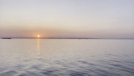 landscape shot of the sun setting over a calm ocean, sun a bright orange colour