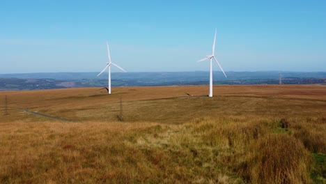 low angle aerial view of renewable energy wind turbine farm with electricity pylons and countryside road 4k and blue sky background 4k