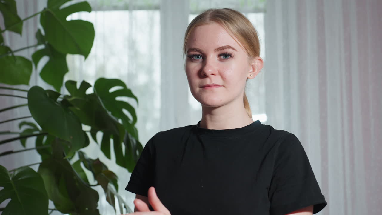 Close up of massage therapist in black shirt rubbing hands together while standing beside large leafy indoor plant, with natural light streaming through sheer curtain in peaceful setting