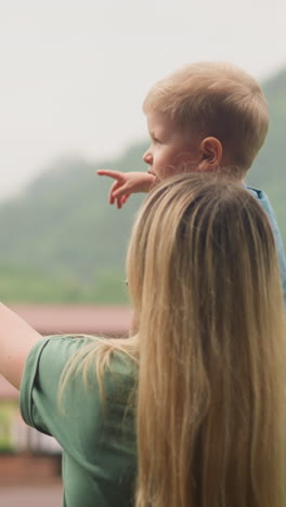 mother and toddler boy enjoy amazing green valley with mountain view standing on hotel room balcony at highland hotel close view slow motion