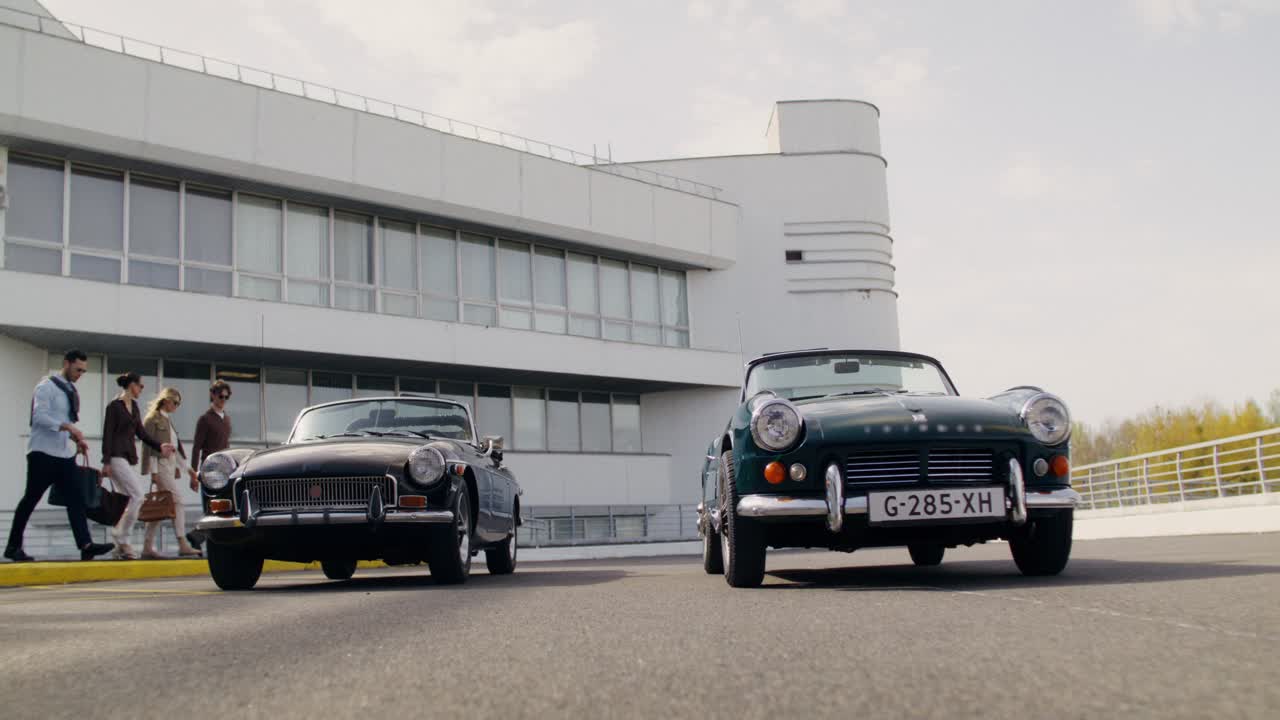 Group of friends by vintage cars in front of a modern building
