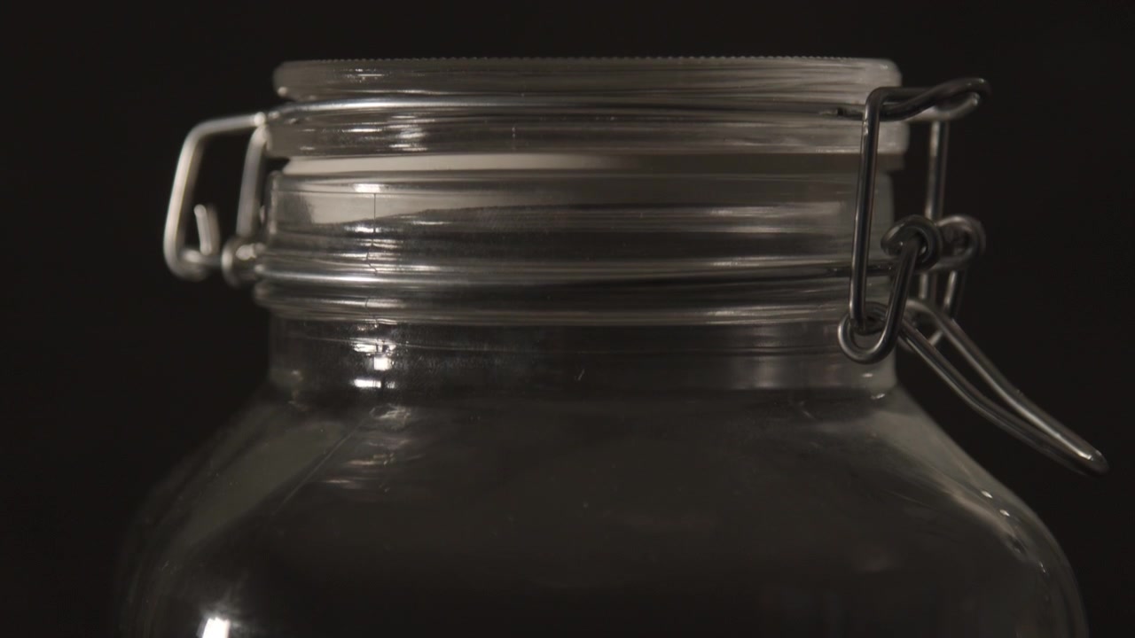 Naheinstellung: Aufwärtsneigung eines Weckglases mit Metallbügel vor schwarzem Hintergrund.
