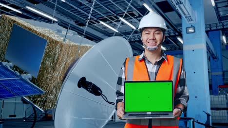 ingeniero sosteniendo una computadora portátil con pantalla verde en una fábrica de satélites