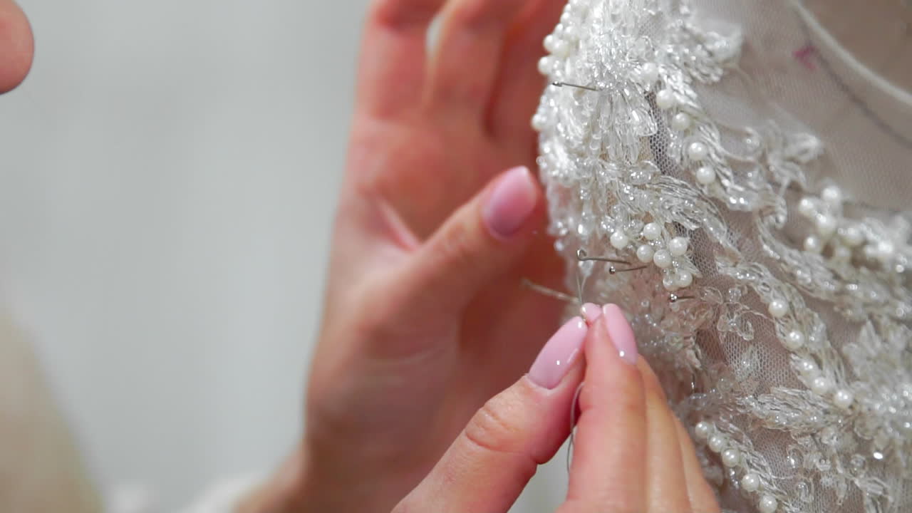 Close-up fashion designer for brides in his Studio pins needles lace wedding dress. Seamstress creates an exclusive wedding dress. Secure with pins and needles outline. Small private business. Sew rhinestones and crystals to the dress thread and needle. Jewelry work.