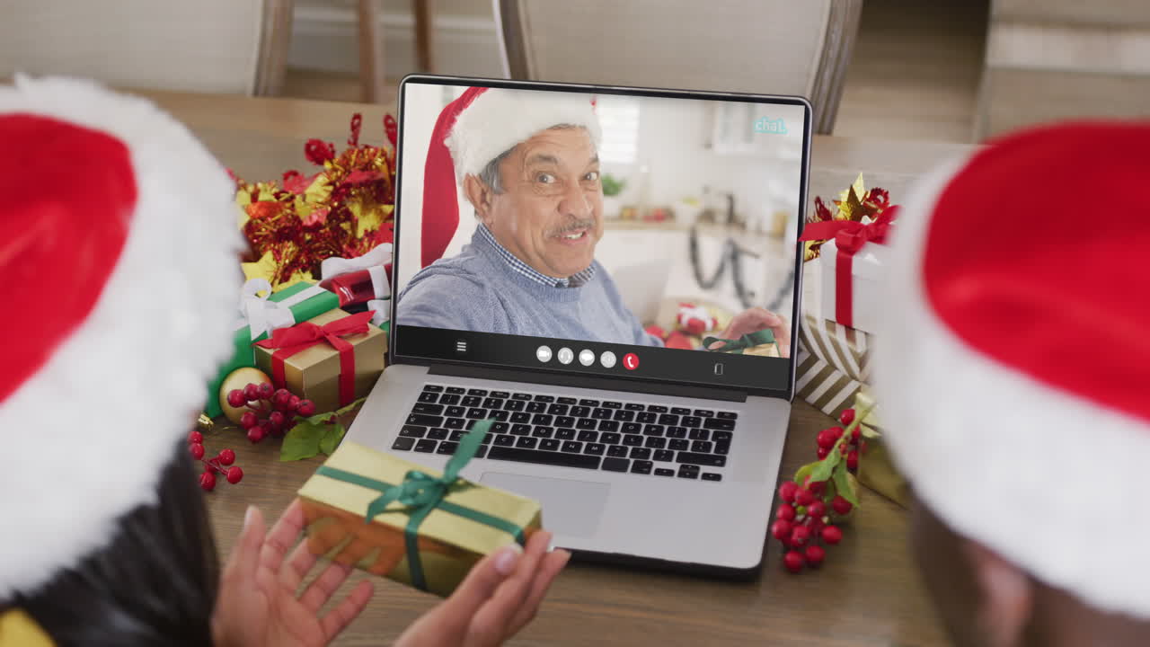 pareja diversa con sombreros de santa teniendo llamada de video portátil con un hombre biracial feliz