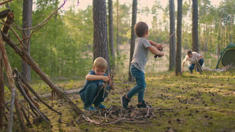 two boys collect sticks in the woods for a large family campfire against the backdrop of a tent and a lake. family is going to light a fire for camping and frying marshmallows