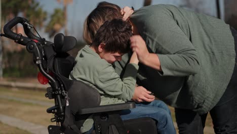 a child in a wheelchair hugging their mother in a park