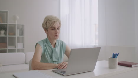 middle-aged-woman-is-talking-online-by-video-call-on-notebook-sitting-at-home-modern-technology-of-communication