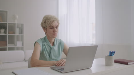 middle-aged woman is talking online by video call on notebook sitting at home modern technology of communication