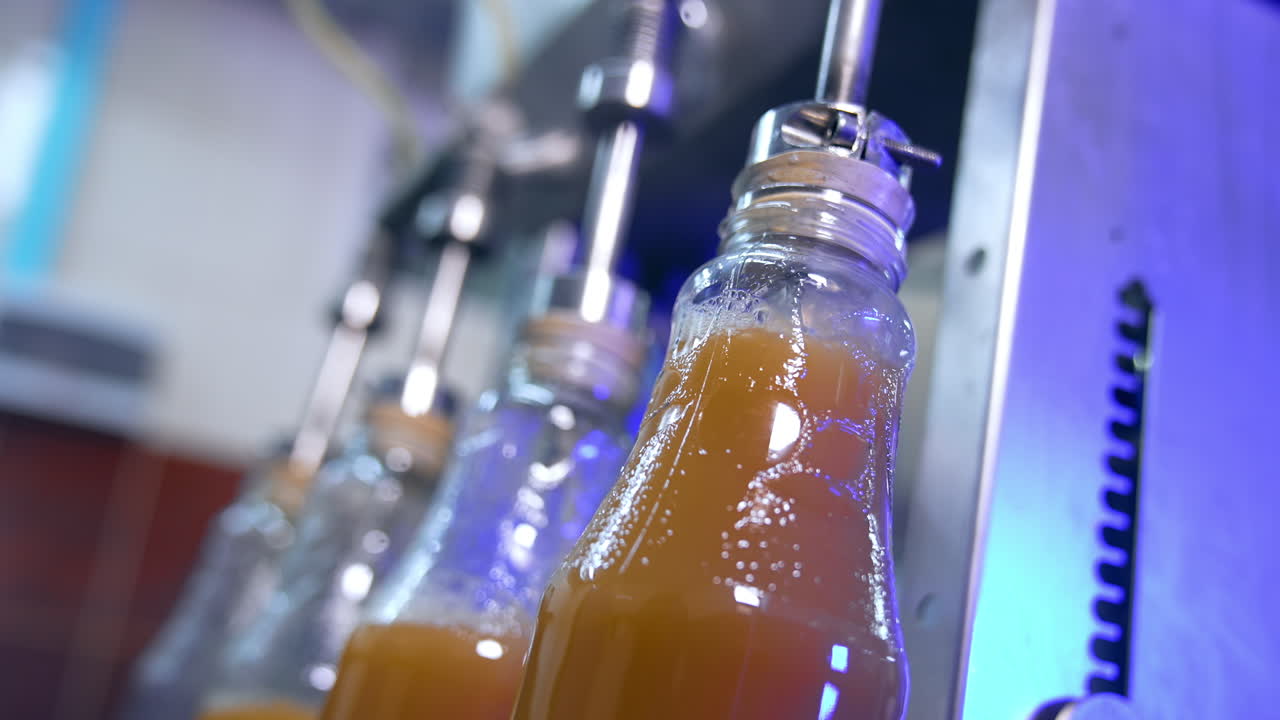 Few glass bottles being filled full with freshly-made juice. Automated technological process of juice manufacturing. Close up.