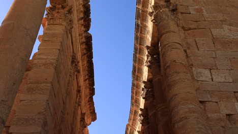 Low-angle-shot-of-Sbeitla-Roman-ruins-against-a-clear-blue-sky,-warm-sunlight-illuminating-the-ancient-stones