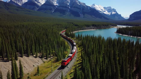 red train winding through mountainous forest and river landscape