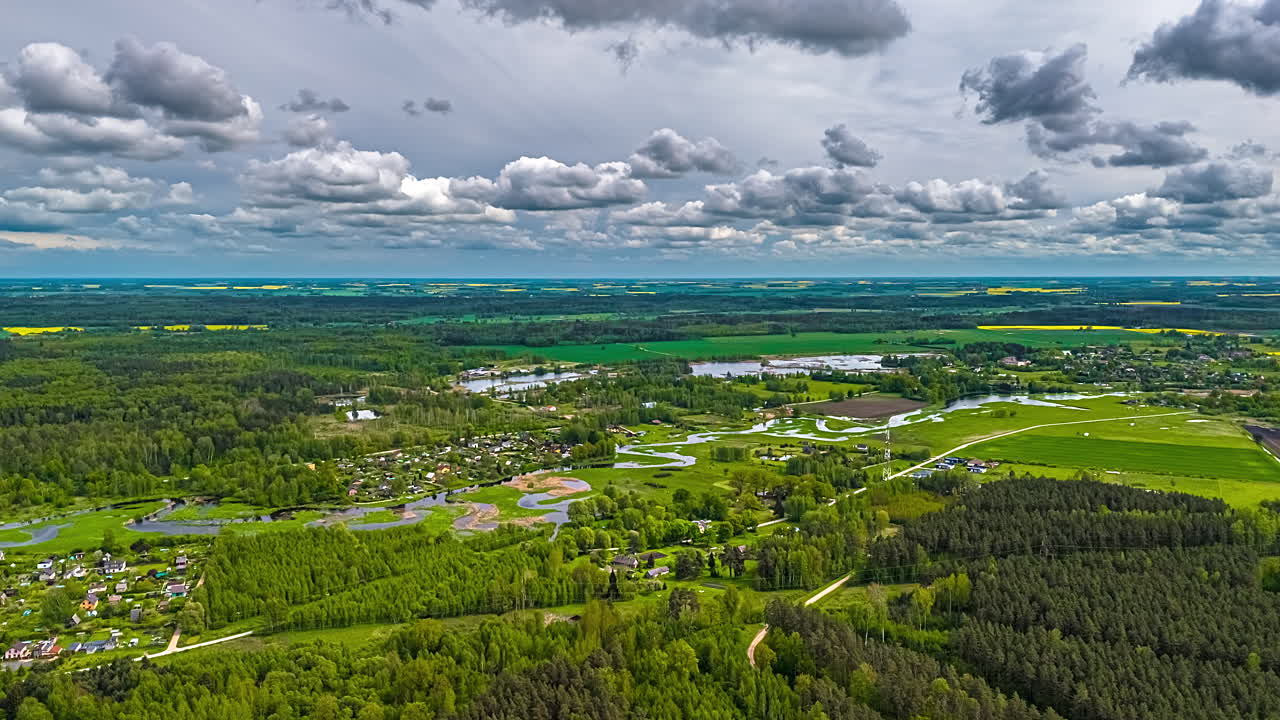 Forest village landscape with dramatic clouds and meandering river in aerial timelapse