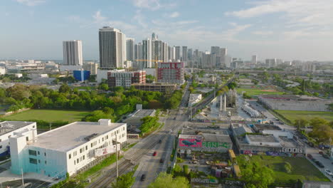 Aerial-panoramic-view-of-large-city.-Vehicles-driving-on-road-and-crossing-railway-track.-High-rise-apartment-buildings-in-background.-Miami,-USA