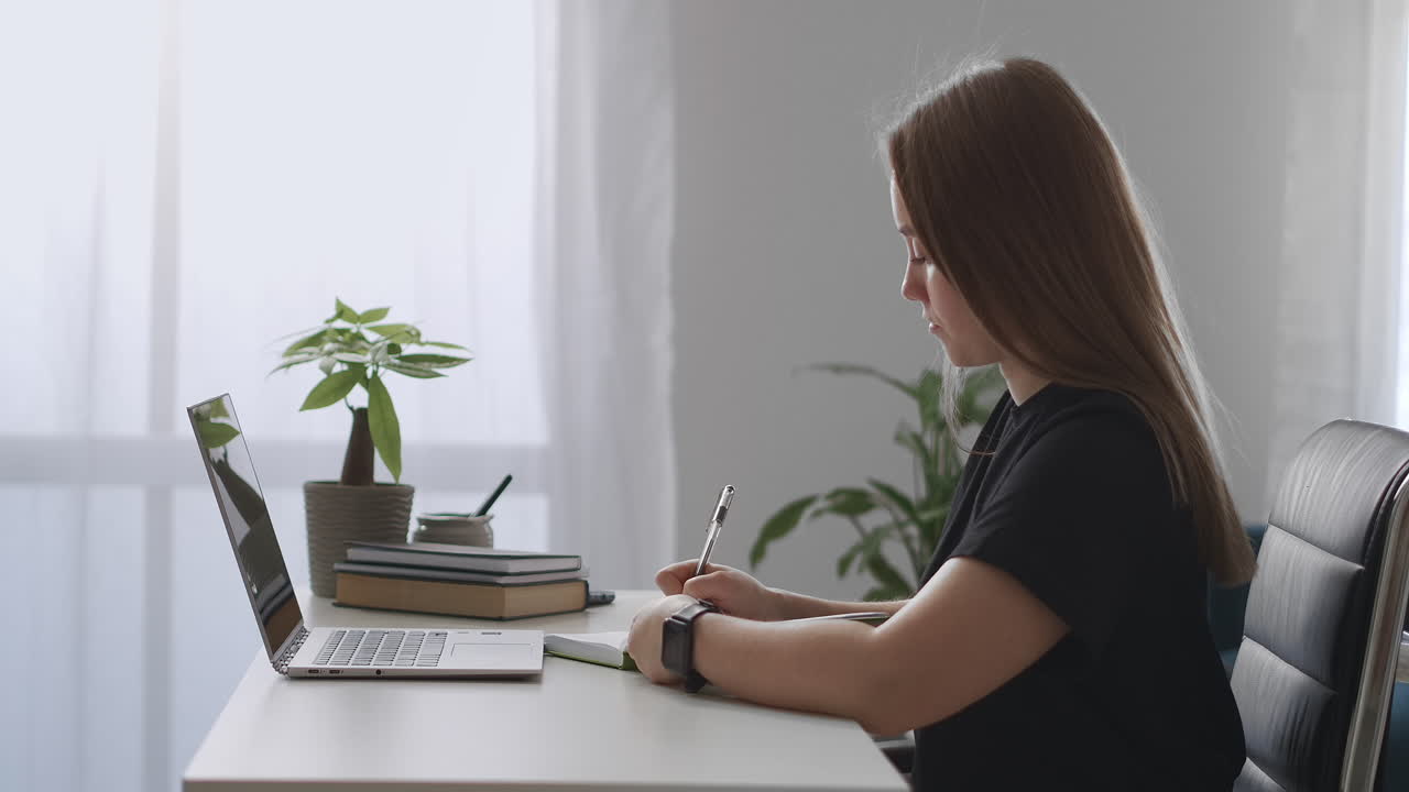 mujer está viendo un seminario web de capacitación en línea tomando notas en un cuaderno aprendiendo desde casa educación a distancia y desarrollo profesional sentada en una mesa con una computadora portátil