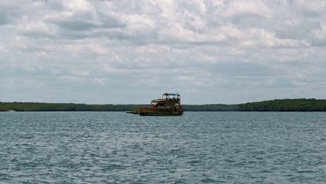 Slow-motion-shot-of-a-tourist-transport-ship-sailing-towards-Restinga-beach-on-a-large-slow-moving-river-near-coastal-town-of-Barra-do-Cunhaú-in-Rio-Grande-do-Norte,-Brazil-on-a-summer-day