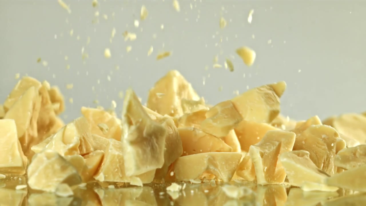 Pezzi di cioccolato bianco che cadono al rallentatore su superficie riflettente