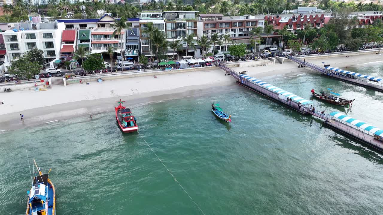 Aerial footage captures longtail boats near a pier in Phuket, showcasing vibrant beachfront activity and scenic coastal views