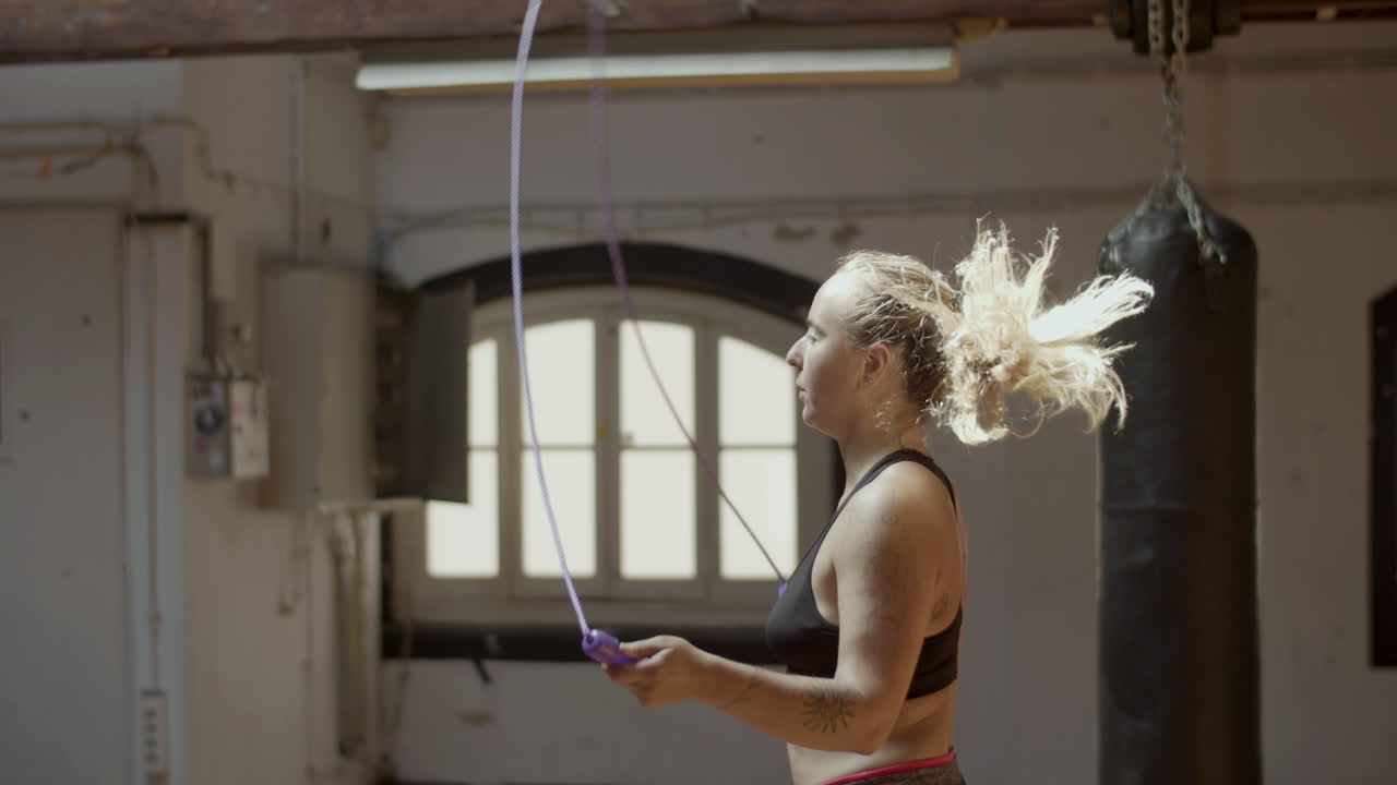 Side view of young serious woman jumping rope in gym